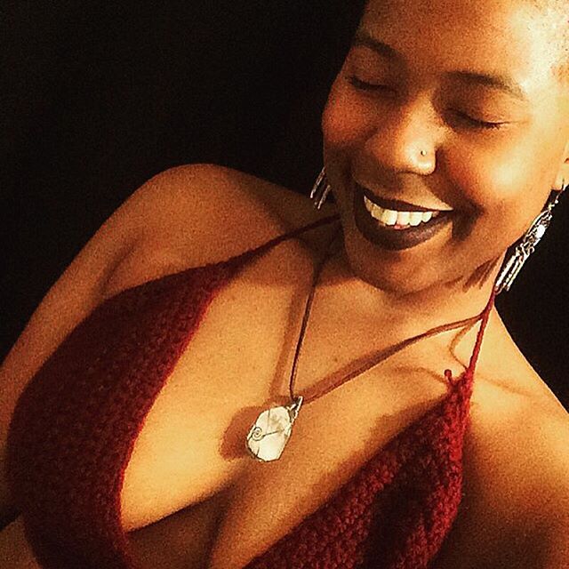 Smiling woman with eyes closed, wearing a pendant and deep red top