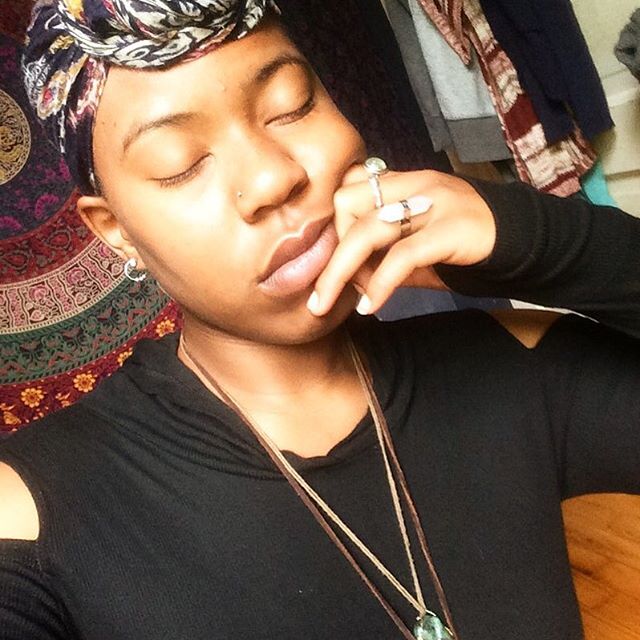 Eyes closed, hand near mouth, wrapped in headscarf and layered jewelry
