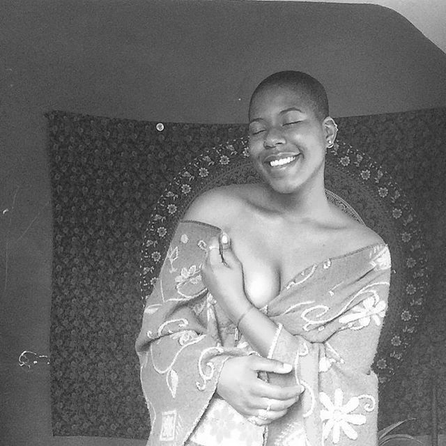 Smiling figure draped in fabric, seated in front of a sacred spiral