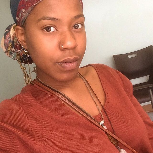 Woman in rust-colored top and headscarf, looking directly into camers