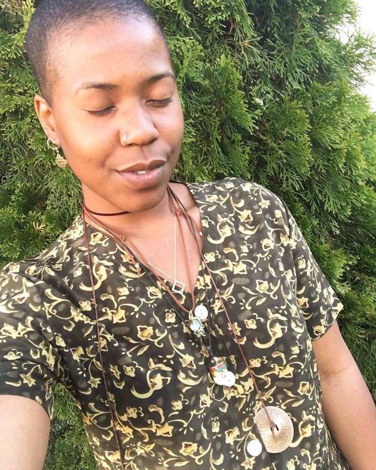 Woman standing with eyes closed, wearing patterned top, standing before green foliage