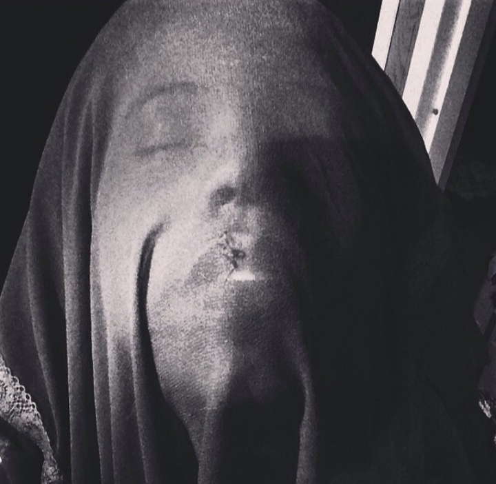 A face pressed beneath a dark veil or cloth, eyes closed and lips visible through the fabric. The image is in black and white and evokes a dreamlike or ghostly feeling.