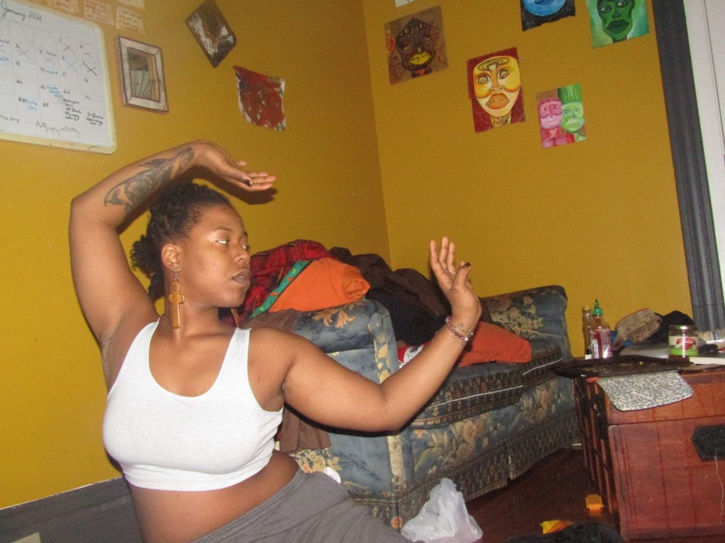 A woman poses gracefully in a dance-like stance in a warmly colored room.