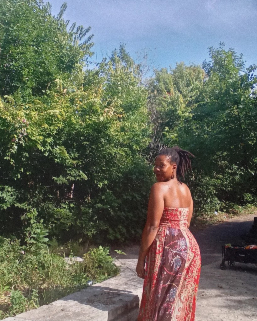 Woman in patterned dress walking away on a forest path, looking back over her shoulder