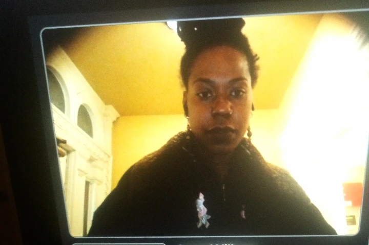 Woman tith top bun and coat, standing in warm yellow light, looking straight ahead