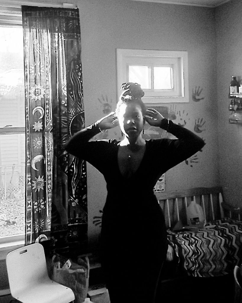 Black and white image of a woman standing with arms raised in front of a lit window